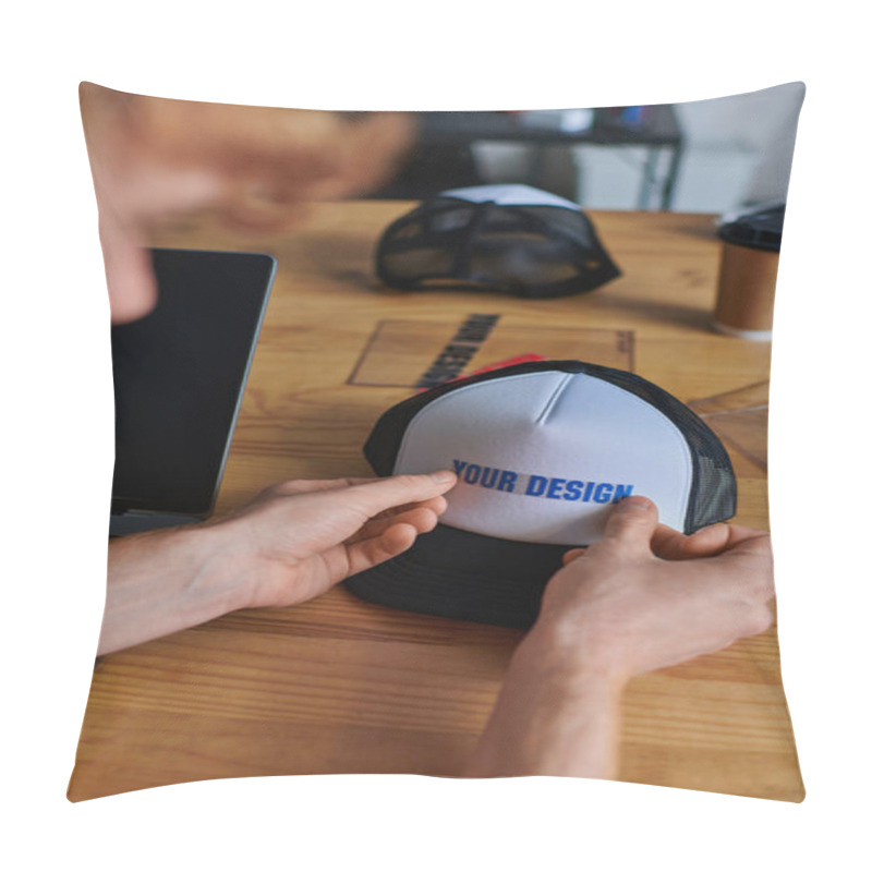 Personality  Cropped View Of Blurred Young Craftsman Holding Printing Layer Near Snapback On Table And Laptop With Blank Screen In Print Studio, Hands-on Entrepreneurship Concept  Pillow Covers