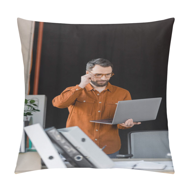 Personality  Serious Bearded Businessman Adjusting Stylish Eyeglasses And Looking At Laptop Near Folders, Notebooks And Documents On Office Desk On Blurred Foreground Pillow Covers