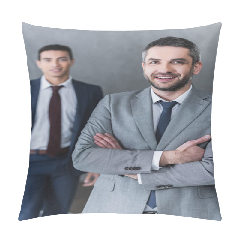 Personality  Confident Businessman Standing With Crossed Arms And Smiling At Camera While Young Colleague Standing Behind Pillow Covers