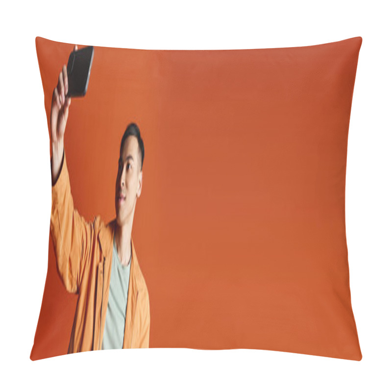 Personality  A Handsome Asian Man In Stylish Attire Holding A Cell Phone Up In The Air Against An Orange Background. Pillow Covers