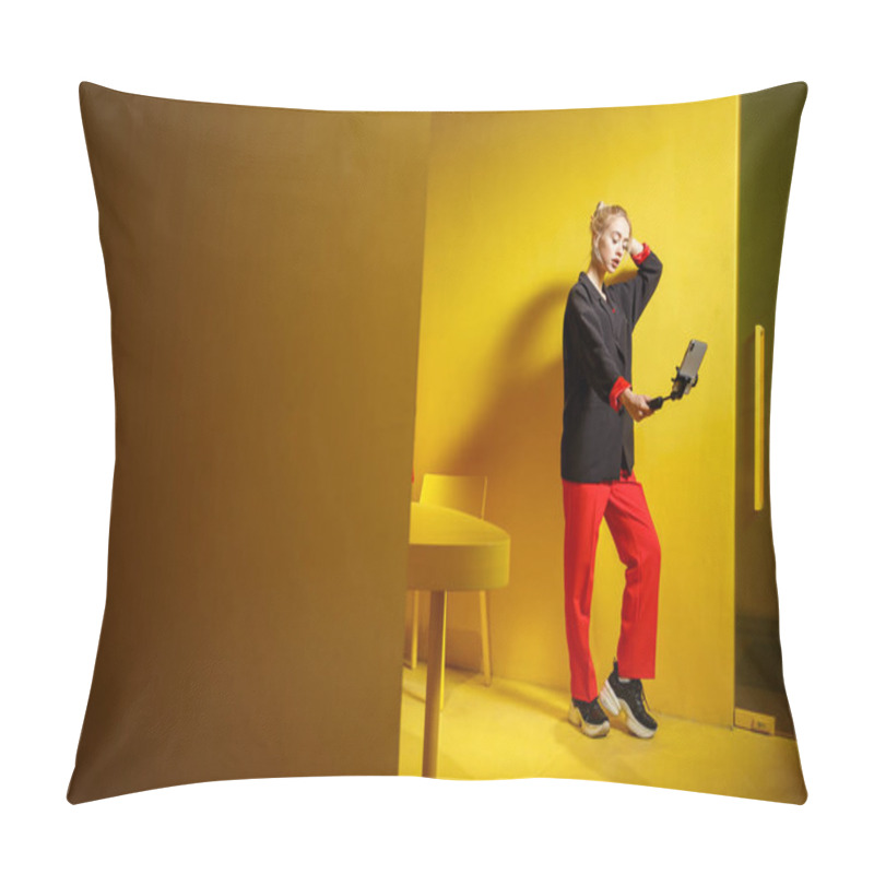 Personality  Fashion Young Girl Blogger Dressed In Red Trousers And Black Jacket Takes A Selfie On Her Smartphone In The Room With Yellow Walls And Furniture Pillow Covers