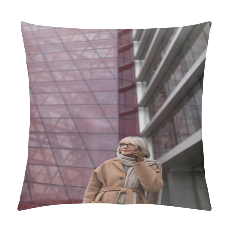 Personality  An Elderly Woman Wearing A Stylish Tan Coat And Scarf Engages In A Cheerful Phone Call Near A Contemporary Glass Building. The Urban Landscape Reflects Modern Architecture And Design. Pillow Covers