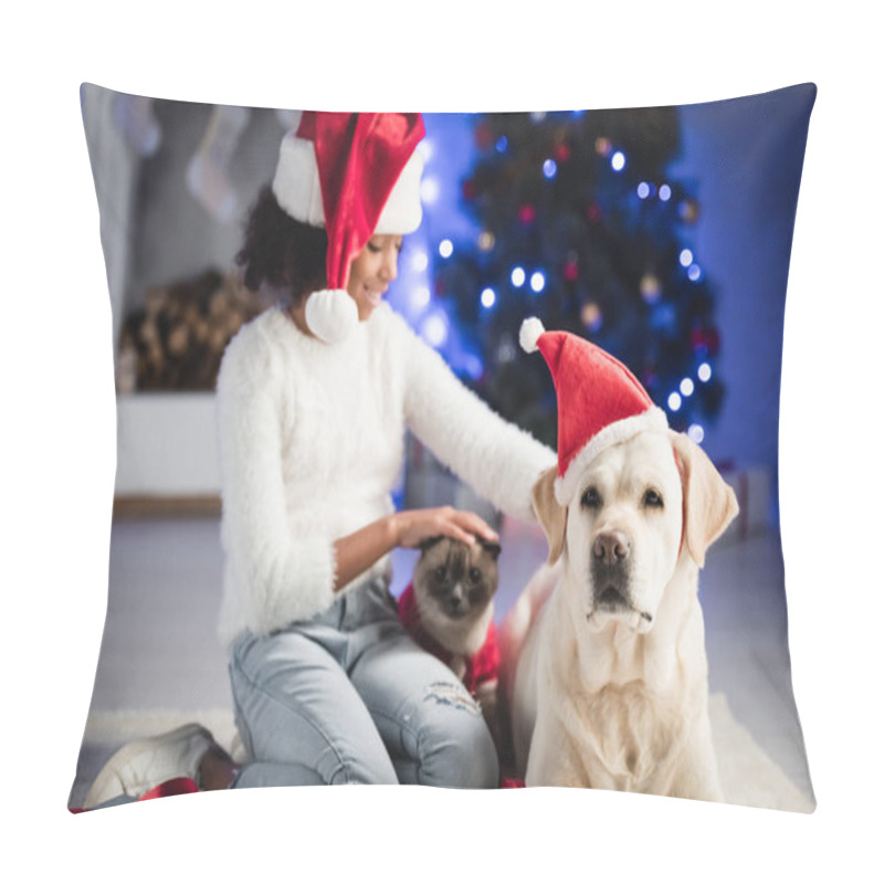 Personality  Positive African American Girl In Santa Hat, Stroking And Looking At Cat And Dog, While Sitting On White Rug On Blurred Background Pillow Covers