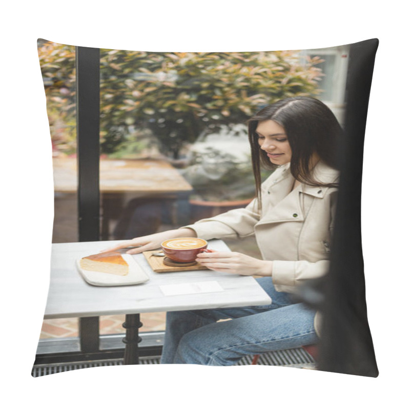 Personality  Happy Woman With Long Hair Sitting In Leather Jacket Next To Window And Bistro Table While Holding Cup Of Cappuccino With Coffee Art And Looking At Cheesecake Inside Of Modern Cafe In Istanbul  Pillow Covers