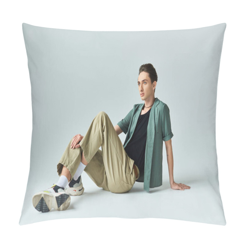 Personality  A Young Queer Person In A Tan Shirt And Khaki Pants Sits On The Floor In A Thoughtful Pose In A Studio Setting Against A Grey Background. Pillow Covers