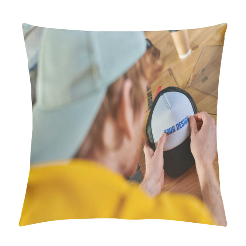 Personality  Blurred Young Designer Holding Printing Layer Near Snapback While Working Near Blurred Coffee To Go On Table In Print Studio, Hands-on Entrepreneurship Concept  Pillow Covers