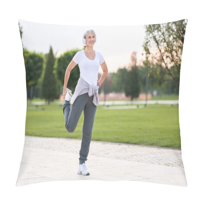 Personality  Photo Of Mature Active Positive Woman In Wireless Headphones Doing Legs Stretching Exercises With Smile, Warming Up Muscles Before Routine Workout And Jogging Outside In City Park In Sunny Morning Pillow Covers