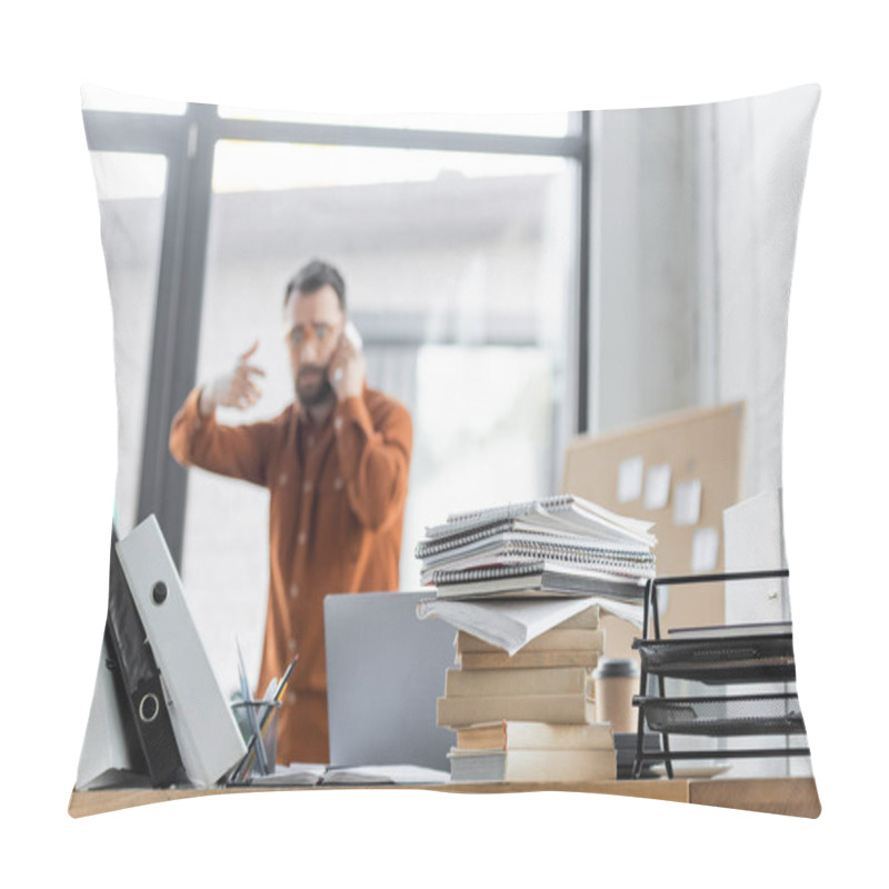 Personality  Selective Focus Of Office Desk With Pile Of Books, Notebooks, Folders And Laptop Near Busy Businessman Gesturing While Talking On Mobile Phone And Solving Problem On Blurred Background Pillow Covers