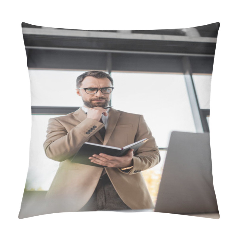 Personality  Low Angle View Of Thoughtful Businessman In Eyeglasses And Stylish Blazer Standing With Notebook And Pen And Looking At Laptop In Office On Blurred Foreground Pillow Covers