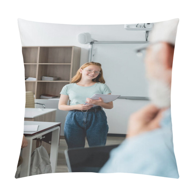 Personality  Smiling Schoolgirl Holding Notebook Near Blurred Teacher In Classroom  Pillow Covers