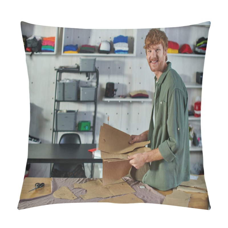 Personality  Smiling Young Redhead Craftsman Looking At Camera While Holding Sewing Patterns Near Scissors And Fabric On Table In Print Studio, Multitasking Business Owner Managing Multiple Project Pillow Covers