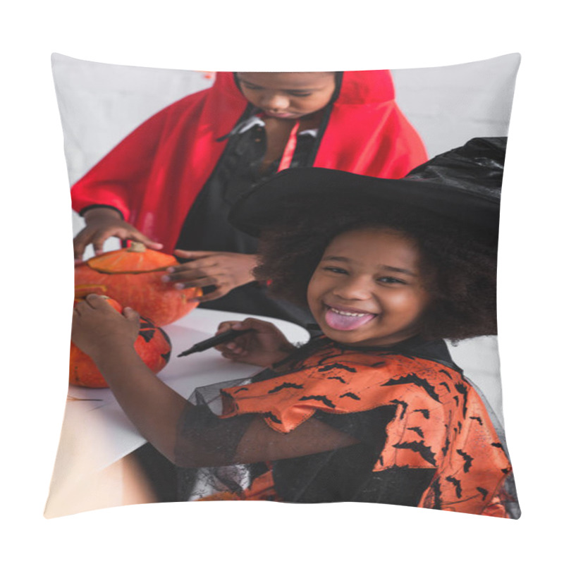 Personality  happy african american girl in witch costume sticking out tongue while drawing pumpkin on near blurred brother  pillow covers