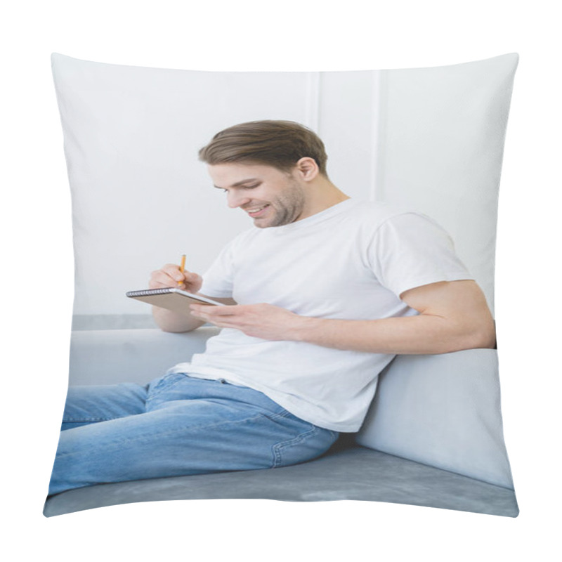 Personality  Happy Man In White T-shirt Writing In Notebook While Sitting On Couch At Home Pillow Covers