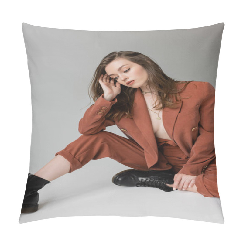 Personality  Full Length Of Sensual And Young Woman With Brunette And Wavy Hair Sitting In Trendy And Oversize Suit With Blazer, Pants And Black Boots, Looking Down On Grey Background, Stylish Model   Pillow Covers