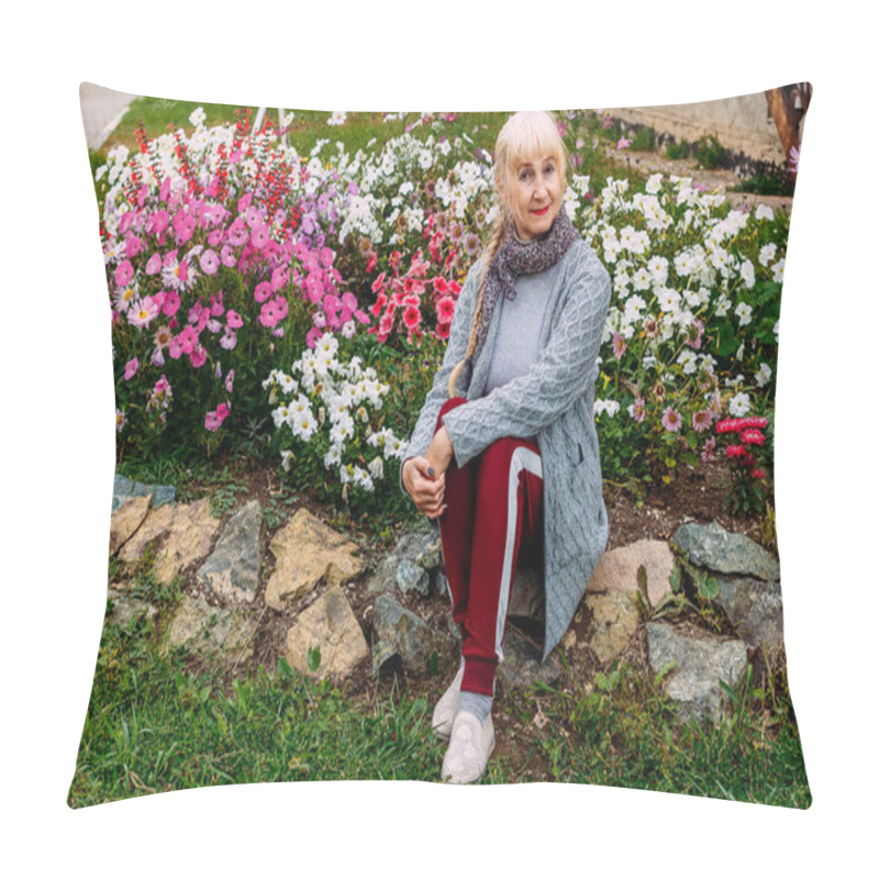 Personality  Fifty-year-old Attractive Blonde Woman In A Gray Cardigan Sitting Near A Flowering Flower Bed With Petunias In The Summer Pillow Covers