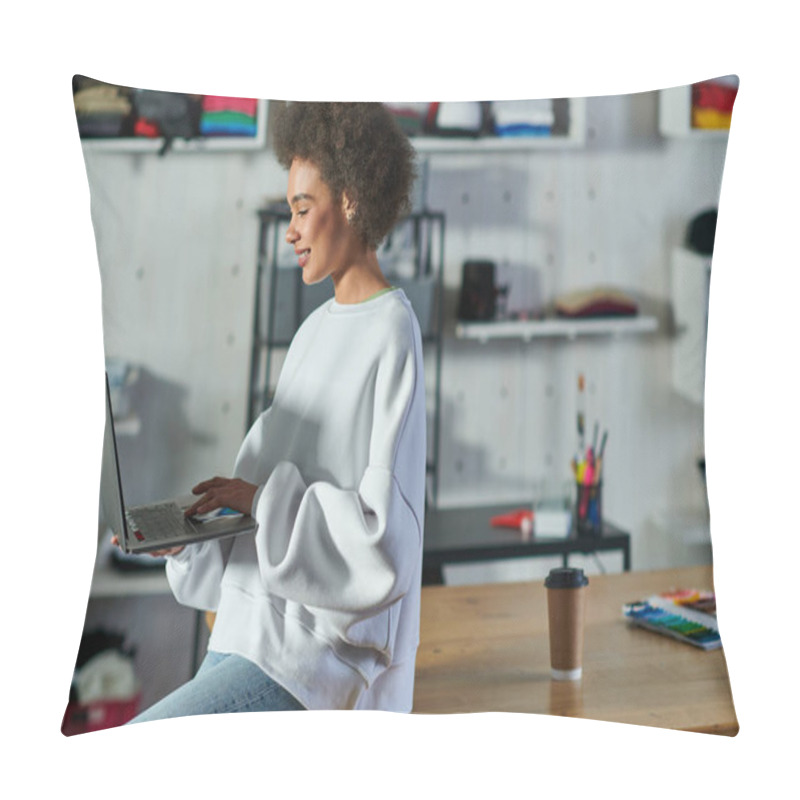 Personality  Positive Young African American Craftswoman In Jeans And Sweatshirt Using Laptop While Sitting Near Coffee To Go On Table In Print Studio, Enthusiastic Business Owner Working In Workshop Pillow Covers