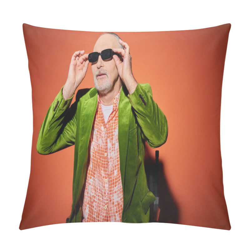 Personality  Positive And Fashionable Aging Concept, Senior Male Model In Green Velour Blazer And Trendy Shirt Looking Away And Adjusting Dark Sunglasses While Sitting On Chair On Red And Orange Background Pillow Covers