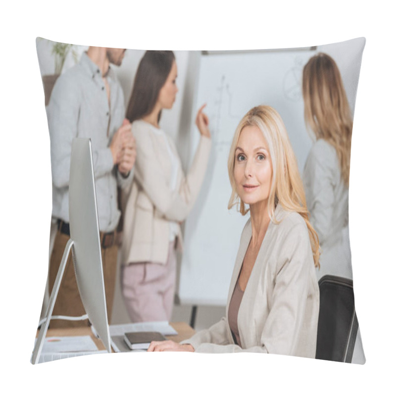 Personality  Mature Businesswoman Using Desktop Computer And Looking At Camera While Young Colleagues Working With Whiteboard Behind Pillow Covers