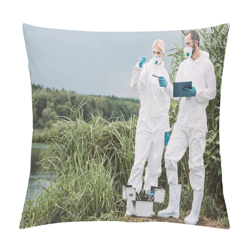 Personality  Male Scientist In Protective Suit And Mask Writing In Clipboard And Pointing While His Female Colleague Examining Sample Of Water In Test Flask Outdoors  Pillow Covers