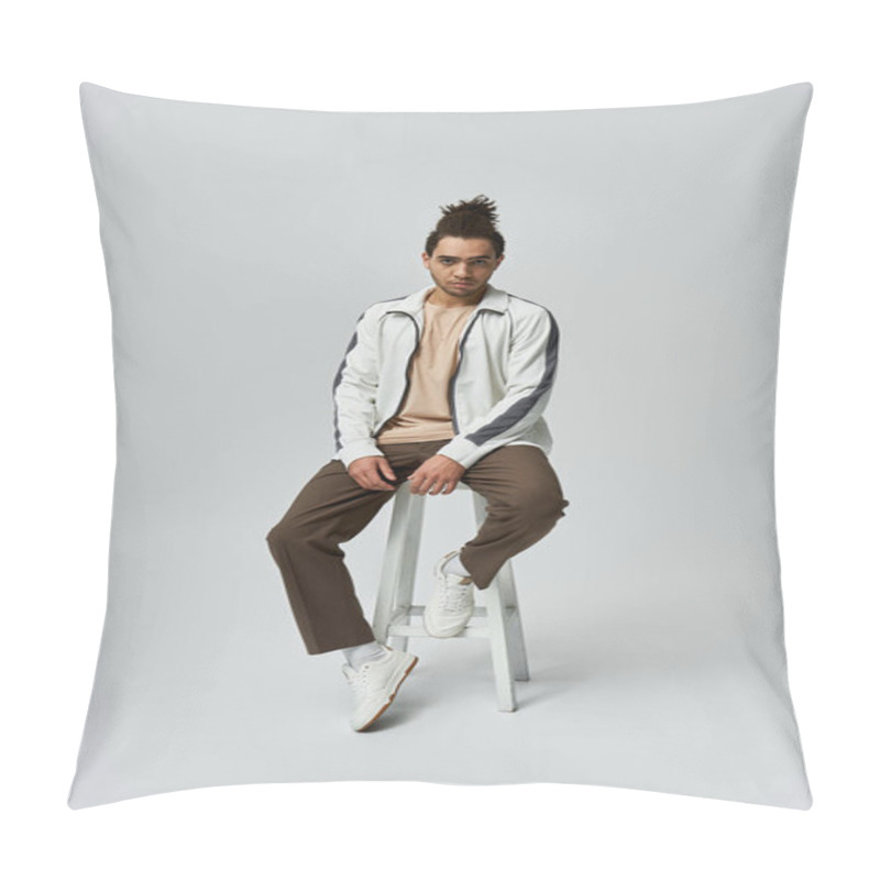 Personality  A Young African American Man Sits Casually On A White Stool, Wearing A White Jacket And Brown Pants, Posing Against A Grey Background. Pillow Covers