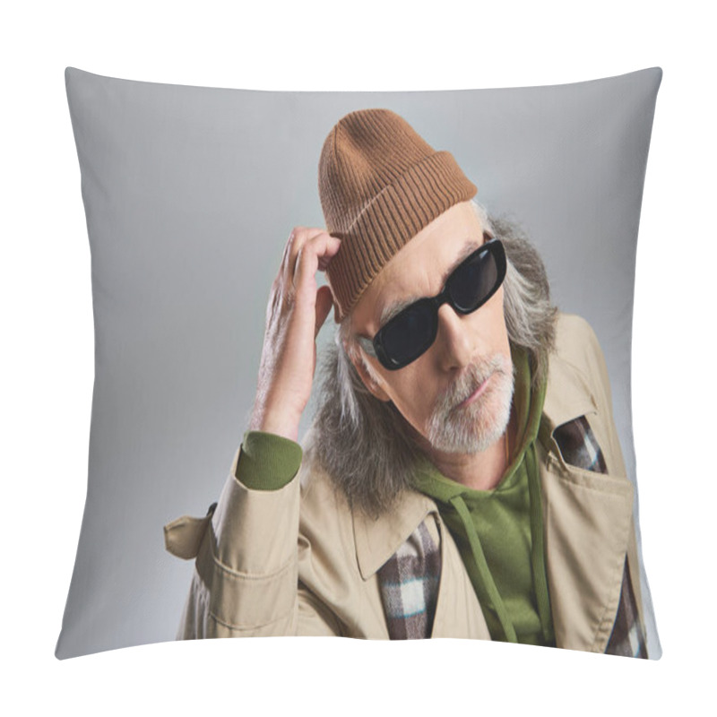 Personality  Portrait Of Thoughtful Elderly Man In Dark Sunglasses And Beige Trench Coat Touching Beanie Hat And Looking At Camera On Grey Background, Hipster Fashion, Stylish And Positive Aging Concept Pillow Covers