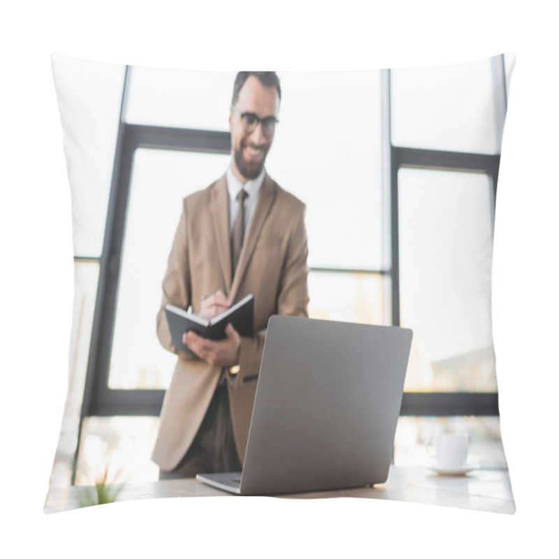 Personality  Positive Bearded Businessman In Eyeglasses, Beige Blazer And Tie Standing Near Laptop And Coffee Cup On Work Desk And Writing In Notebook On Blurred Background Pillow Covers