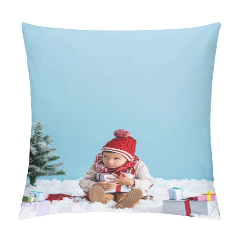 Personality  Boy In Hat And Winter Outfit Sitting On Snow And Holding Gift Box Near Christmas Trees Isolated On Blue Pillow Covers