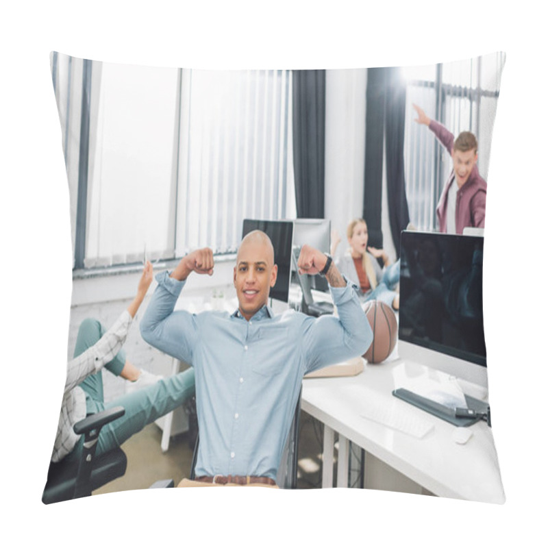 Personality  Happy Young African American Man Showing Biceps And Smiling At Camera While Colleagues Having Fun Behind In Office Pillow Covers