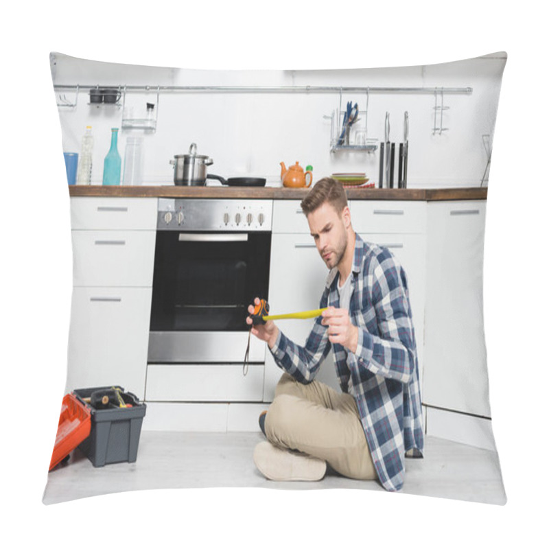 Personality  Full Length Of Focused Young Man Looking At Tape Measure While Sitting Near Oven And Toolbox On Floor Pillow Covers