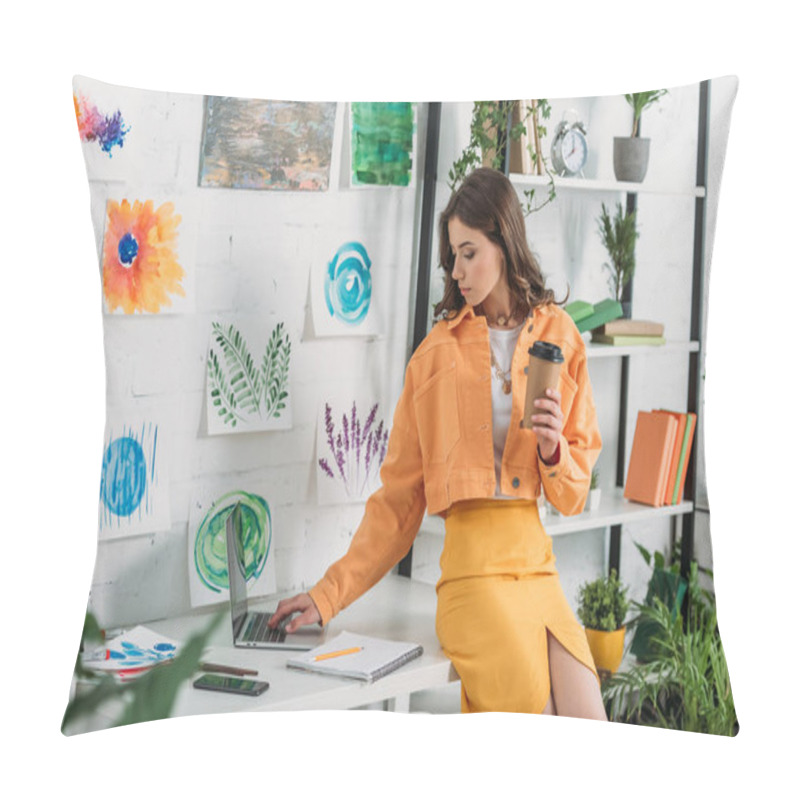 Personality  Pretty Girl Using Laptop And Holding Paper Cup While Sitting On Desk In Room Decorated With Green Plants And Paintings On Wall Pillow Covers