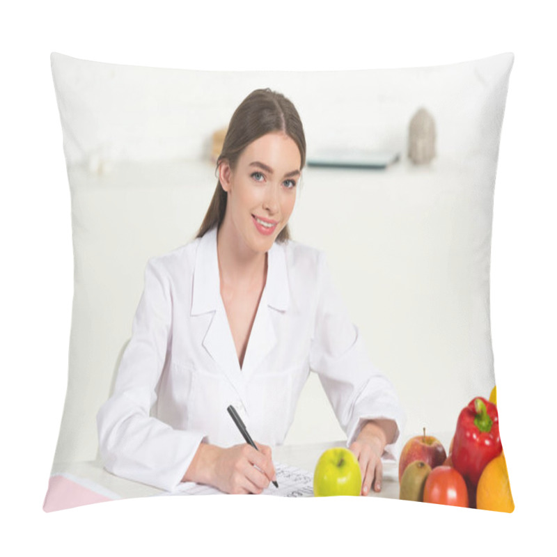 Personality  Smiling Dietitian In White Coat Writing At Workplace With Fruits And Vegetables On Table Pillow Covers