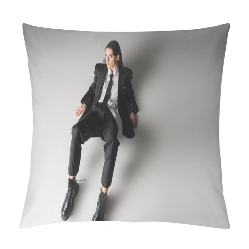 Personality  High Angle View Of Brunette Woman In Black Elegant Suit And Rough Leather Boots Sitting And Looking At Camera On Grey Background Pillow Covers