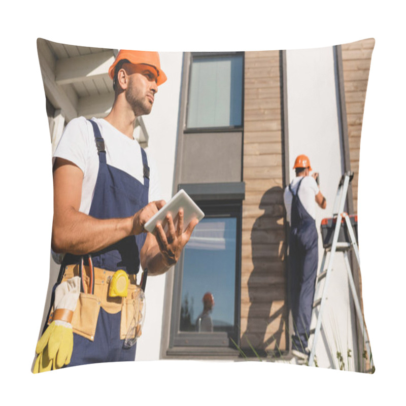 Personality  Selective Focus Of Builder In Uniform And Tool Belt Using Digital Tablet While Colleague Working On Ladder Beside Building   Pillow Covers