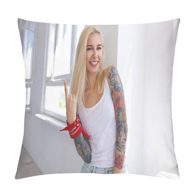 Personality  Indoor Photo Of Young Blonde Long Haired Female With Tattoos Making Rock And Roll Sign With Raised Hand And Smiling Cheerfully At Camera, Posing In Front Of Big Window Pillow Covers