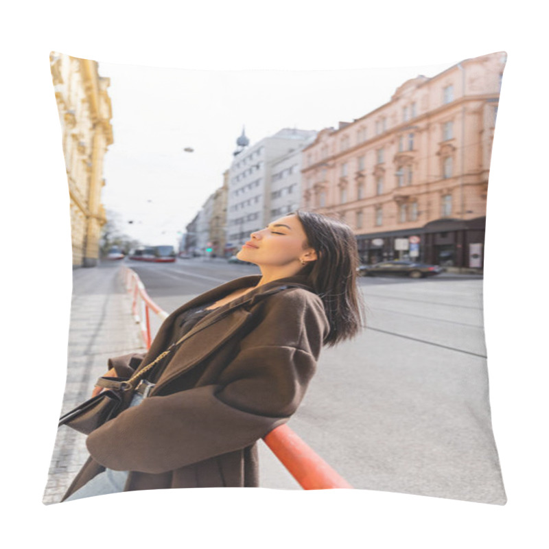 Personality  Side view of brunette woman in coat standing near railing on street in Prague  pillow covers