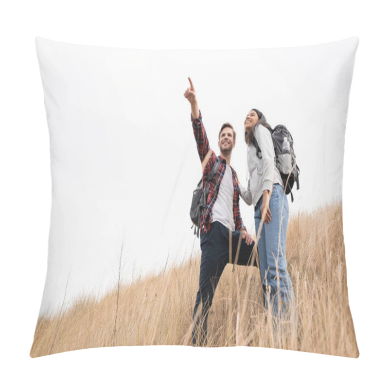 Personality  Low Angle View Of Smiling Man With Backpack Pointing With Finger Away Near African American Woman While Standing On Grassy Hill With Sky At Background  Pillow Covers