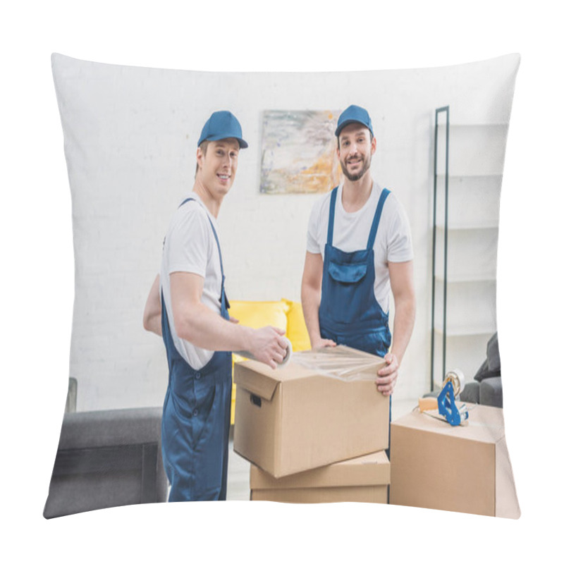 Personality  Handsome Smiling Movers Looking At Camera While Wrapping Cardboard Box With Stretch Film In Apartment Pillow Covers