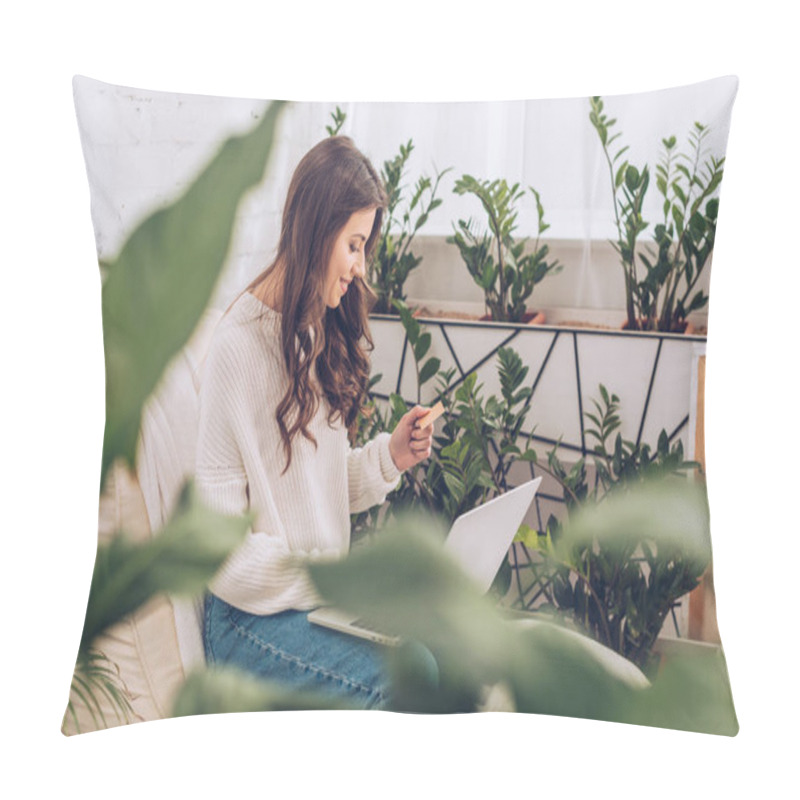 Personality  Selective Focus Of Smiling Woman Holding Credit Card And Using Laptop While Sitting Surrounded By Green Plants  At Home Pillow Covers