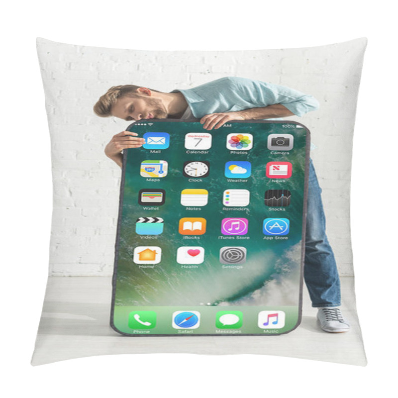 Personality  KYIV, UKRAINE - FEBRUARY 21, 2020: Young Man Kissing Big Model Of Smartphone With Iphone Screen Near White Brick Wall Pillow Covers