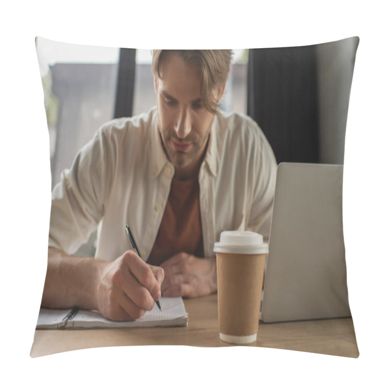 Personality  Focused Young Man Sitting At Desk Near Paper Cup And Laptop And Writing With Pen In Notebook In Modern Office Pillow Covers