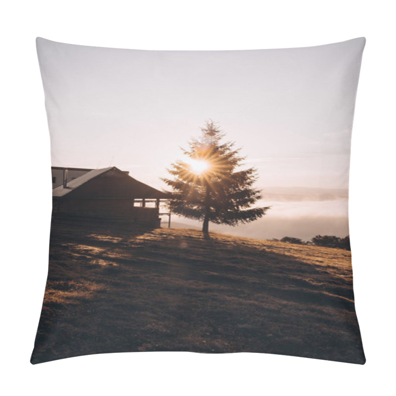 Personality  In this captivating image, the rising sun casts its golden rays through the branches of a solitary tree standing beside a rustic mountain cabin. The early morning light creates a warm and inviting pillow covers