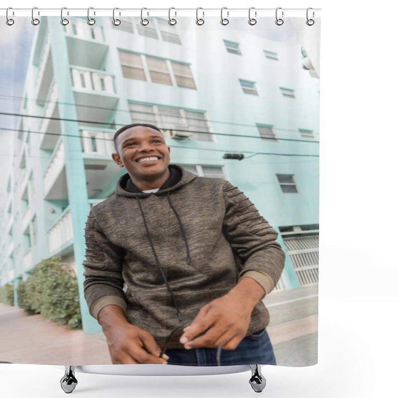 Personality  Low Angle View Of Happy African American Man In Hoodie Holding Stylish Sunglasses While Standing Near Blue Building In Miami  Shower Curtains