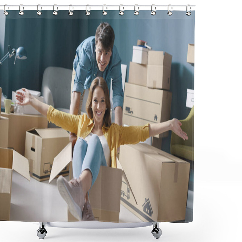 Personality  Cheerful Happy Young Couple Moving In Their New House: She Is Sitting In A Box And Her Boyfriend Is Pushing Her Shower Curtains