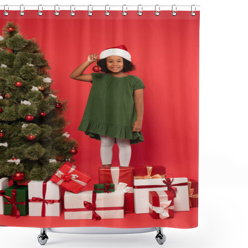 Personality  Smiling African American Child In Santa Hat Holding Christmas Ball Near Presents And Fir Tree On Red Background Shower Curtains