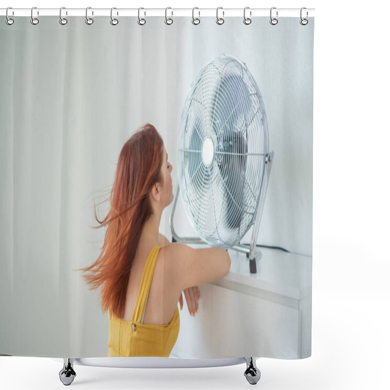 Personality  Portrait Of A Beautiful Red-haired Woman In A Mustard Jumpsuit Enjoying The Cooling Breeze From A Large Electric Fan. A Smiling Girl Freshens Up In The Hot Summer Heat. Hair Develops From The Wind Shower Curtains