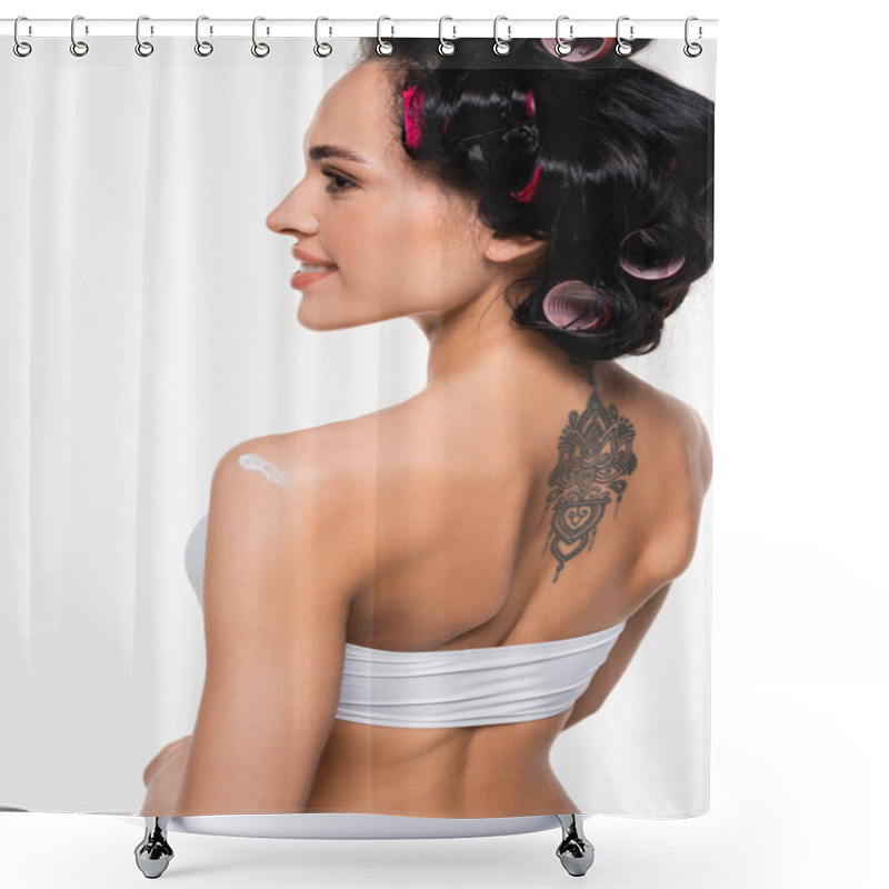 Personality  smiling young woman in curlers and tattoo on back standing with applied cream on shoulder isolated on white shower curtains