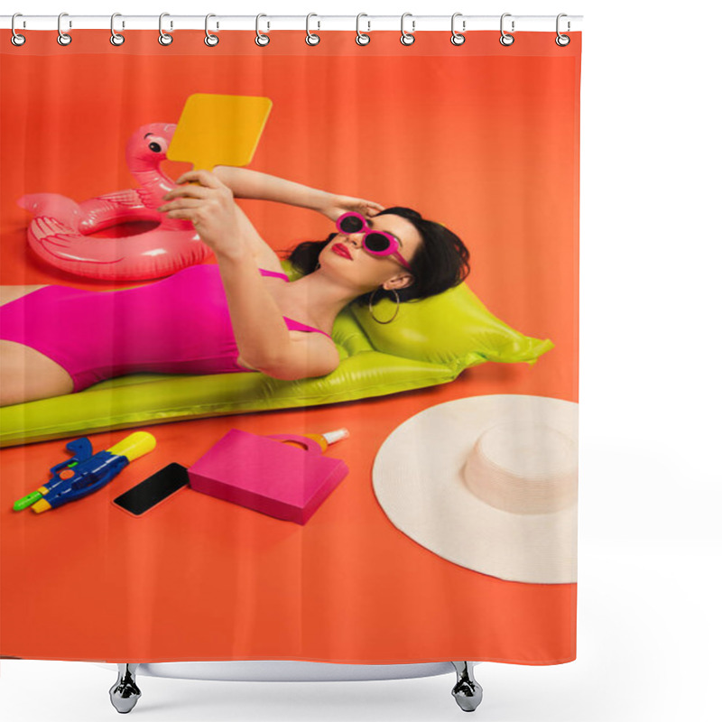 Personality  Woman In Sunglasses And Swimsuit Lying On Inflatable Mattress And Looking At Mirror Near Inflatable Ring And Smartphone With Blank Screen On Orange Shower Curtains