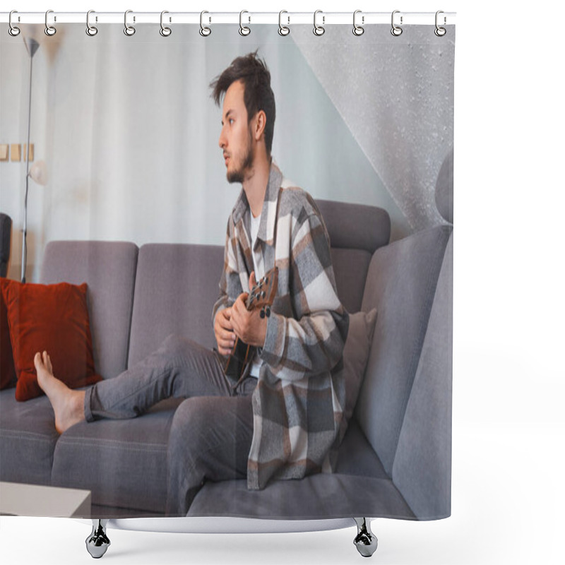 Personality  Man With Talent Sits On A Gray Sofa, Carefully Tuning A Black Ukulele. Musician Is Enjoying The Feeling Of Playing The Ukulele And Immersing Oneself In The Creative Spirit. Shower Curtains