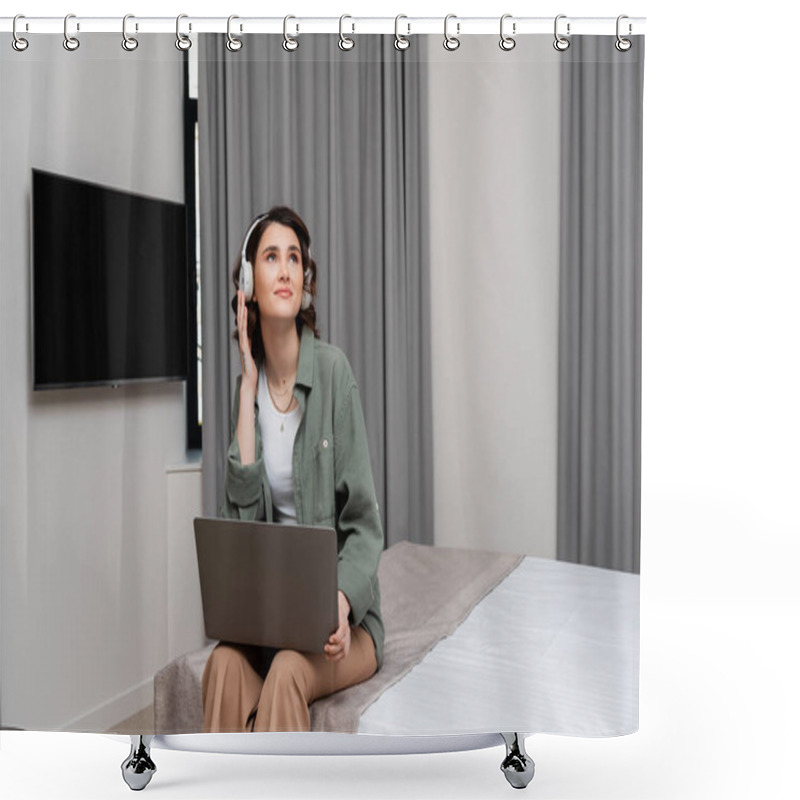 Personality  Positive Young Woman Adjusting Wireless Headphones And Looking Away While Sitting On Bed With Laptop Near Lcd Tv And Grey Curtains During Online Lesson In Hotel Suite, Study And Travel Shower Curtains