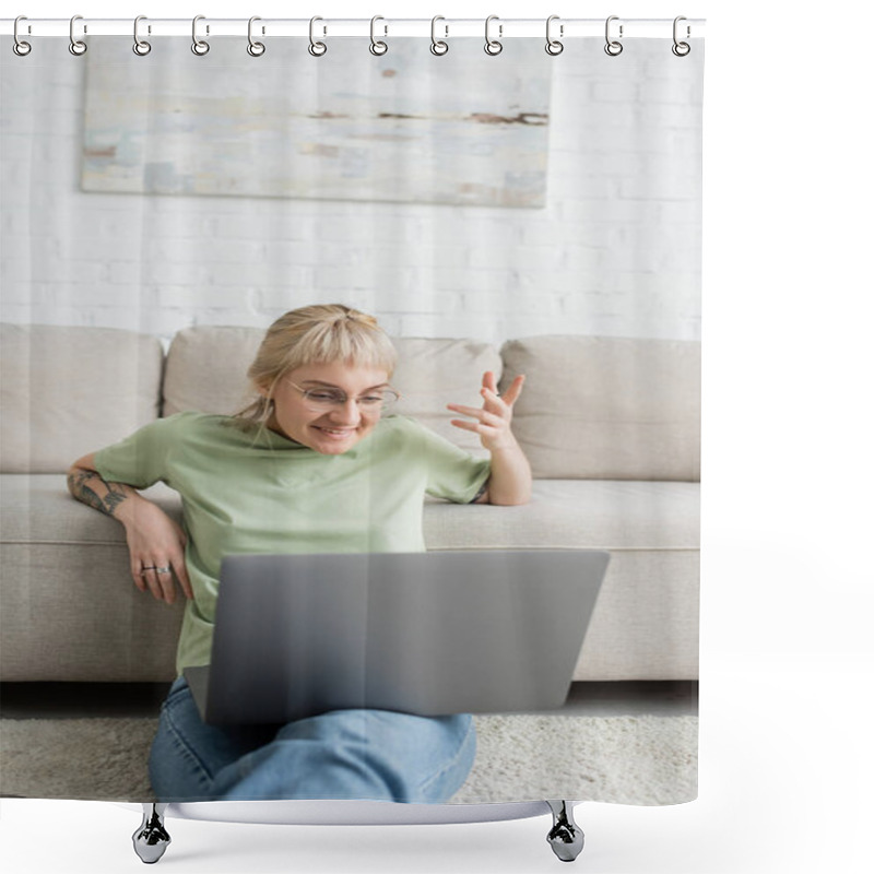 Personality  Tattooed Woman With Blonde And Short Hair, Bangs And Eyeglasses Smiling During Video Call On Laptop While Sitting On Carpet Near Comfortable Couch In Modern Living Room With Paiting On Wall  Shower Curtains